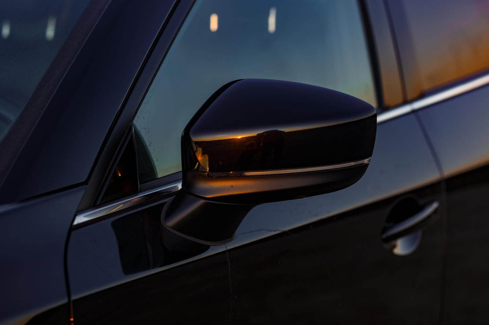 Close do retrovisor e da porta de um carro escuro ao entardecer.